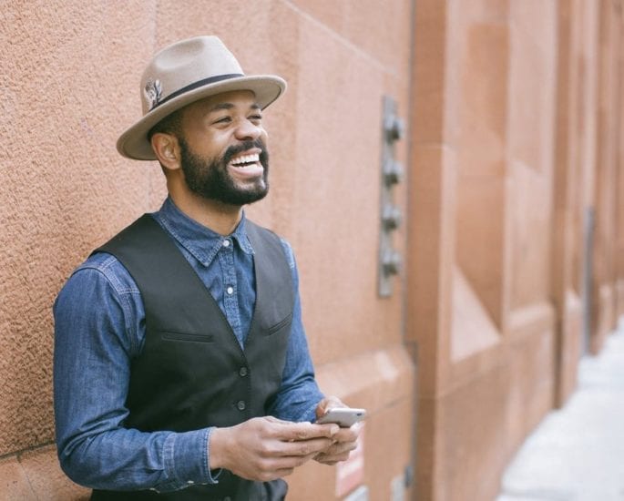 Man in a hat smile as he uses his mobile phone.